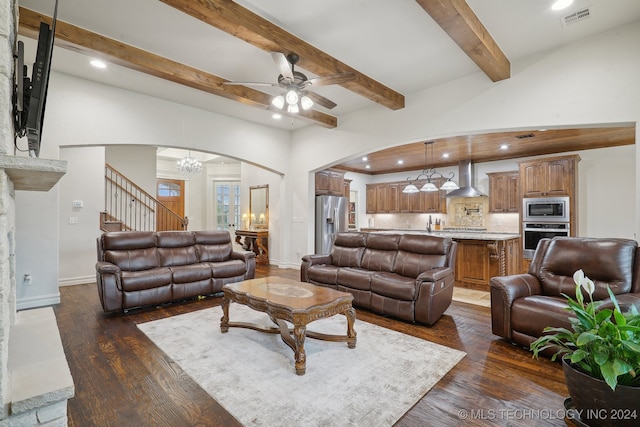 living room featuring ceiling fan with notable chandelier, beam ceiling, and dark wood-type flooring