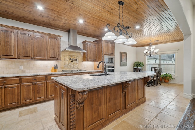 kitchen with a kitchen island with sink, wall chimney range hood, sink, appliances with stainless steel finishes, and decorative light fixtures