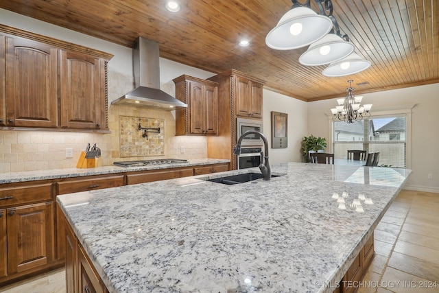 kitchen with a center island with sink, wall chimney exhaust hood, decorative light fixtures, and stainless steel gas stovetop