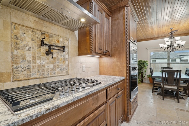 kitchen featuring light stone counters, a notable chandelier, backsplash, custom range hood, and appliances with stainless steel finishes