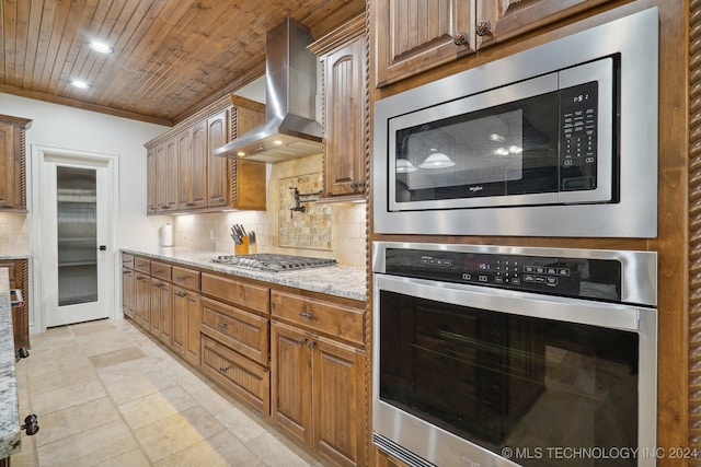 kitchen featuring backsplash, light stone counters, wall chimney exhaust hood, and stainless steel appliances