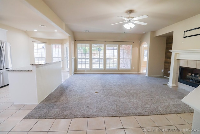 unfurnished living room featuring a tile fireplace, ceiling fan, and light colored carpet