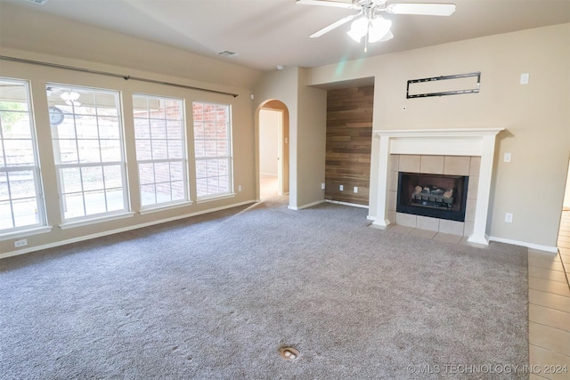 unfurnished living room with a fireplace, a wealth of natural light, wooden walls, and ceiling fan