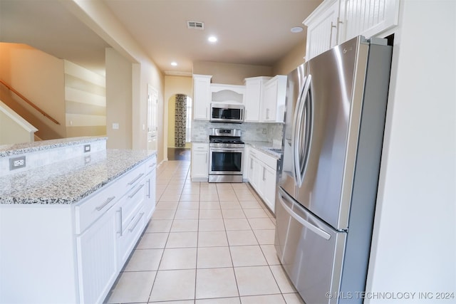 kitchen with stainless steel appliances, white cabinetry, and light stone counters