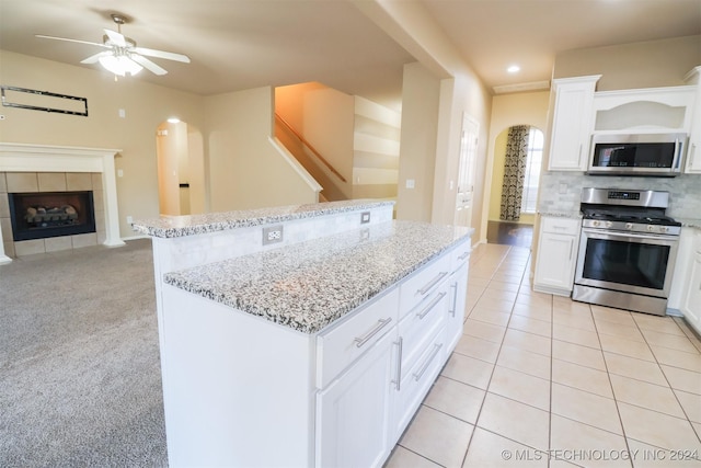 kitchen featuring a tile fireplace, white cabinetry, light carpet, a kitchen island, and appliances with stainless steel finishes