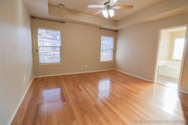 unfurnished room with light hardwood / wood-style floors, a wealth of natural light, a tray ceiling, and ceiling fan