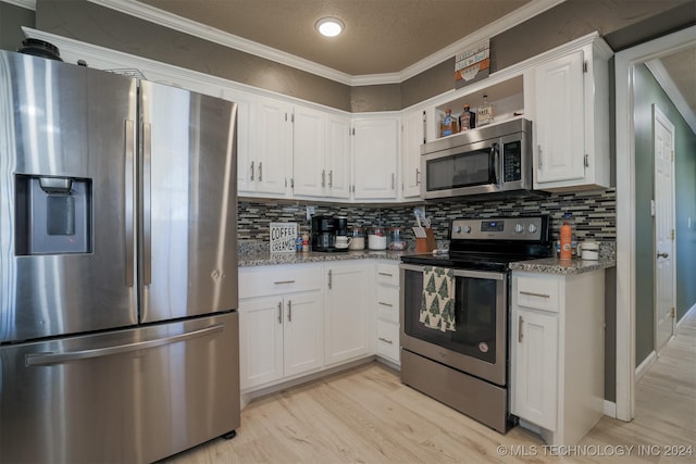 kitchen with white cabinets, stainless steel appliances, light stone counters, and ornamental molding