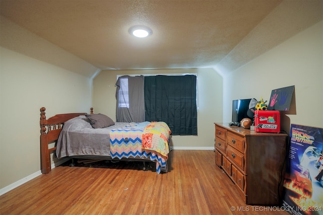 bedroom featuring a textured ceiling, light hardwood / wood-style floors, and lofted ceiling