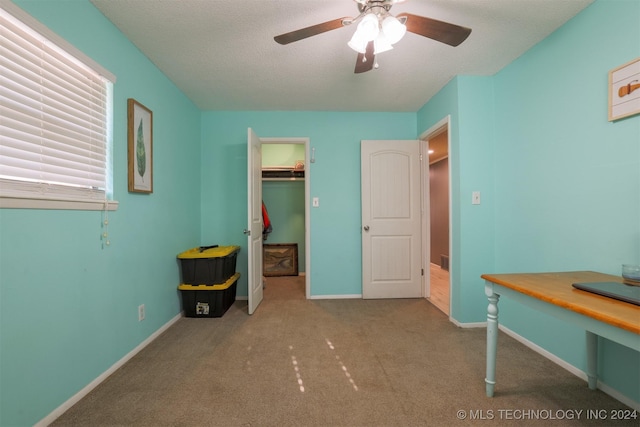 bedroom with a walk in closet, a textured ceiling, light colored carpet, ceiling fan, and a closet