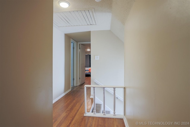 hall featuring a textured ceiling, hardwood / wood-style flooring, and lofted ceiling