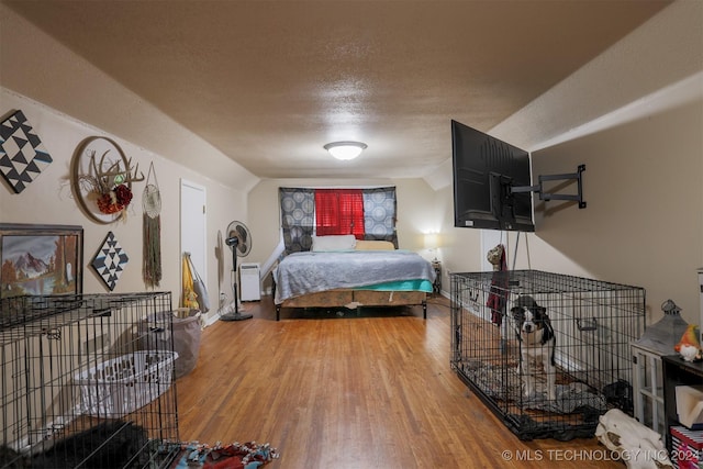 bedroom with a textured ceiling, hardwood / wood-style floors, and vaulted ceiling