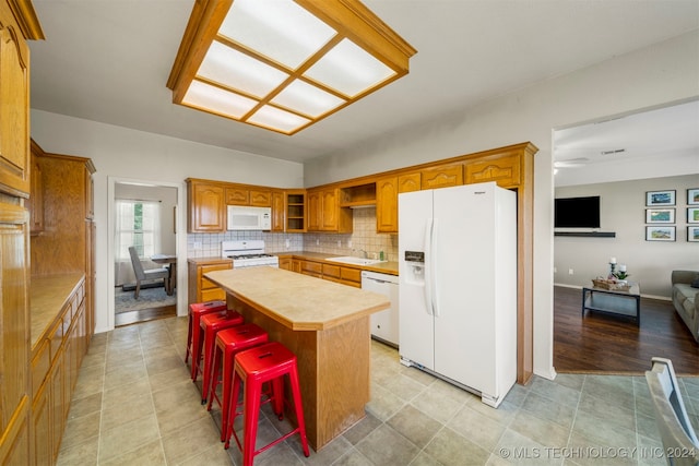 kitchen featuring a kitchen bar, backsplash, white appliances, sink, and a kitchen island