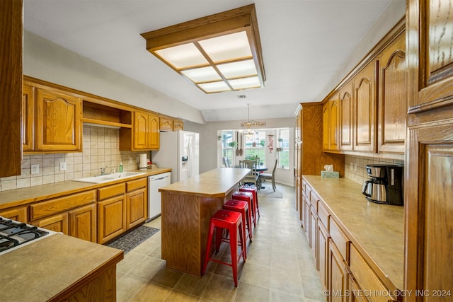 kitchen with a kitchen bar, white appliances, sink, pendant lighting, and a kitchen island