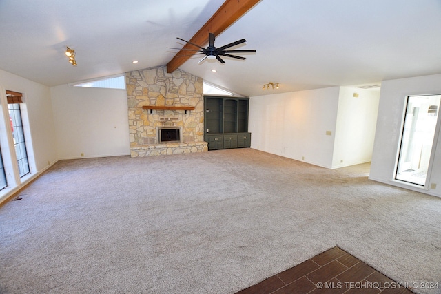 unfurnished living room with carpet flooring, a stone fireplace, ceiling fan, and vaulted ceiling with beams