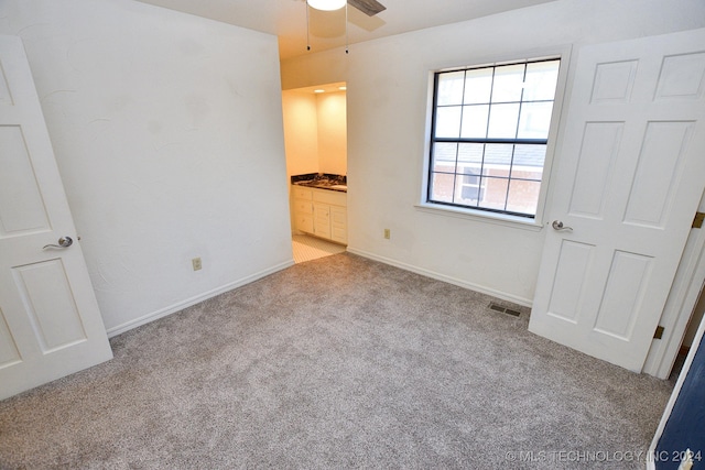 unfurnished bedroom featuring ensuite bath, ceiling fan, and light colored carpet