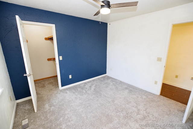 unfurnished bedroom with a walk in closet, light carpet, a closet, and ceiling fan