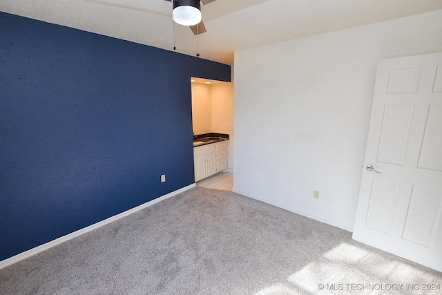 unfurnished bedroom featuring light carpet, ensuite bathroom, and ceiling fan