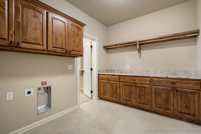 laundry area with electric dryer hookup, light tile patterned floors, and cabinets