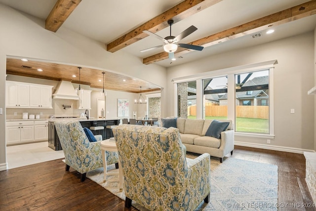 living room with beamed ceiling, ceiling fan with notable chandelier, light wood-type flooring, and sink