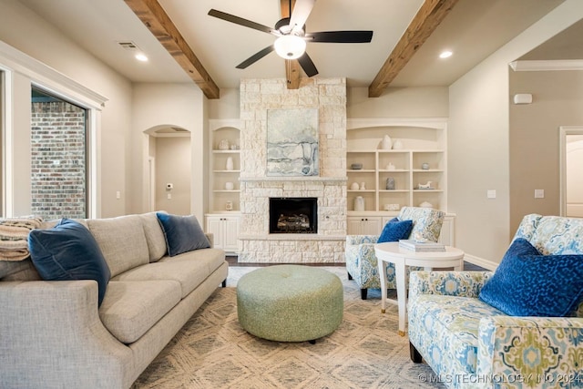 living room featuring beam ceiling, a stone fireplace, ceiling fan, and built in shelves