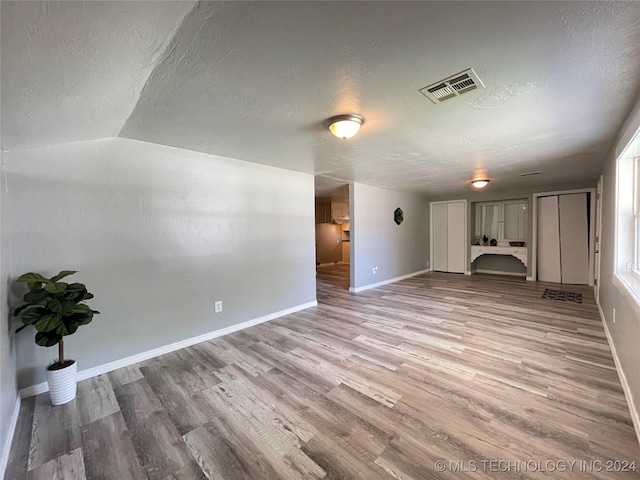 unfurnished living room with a textured ceiling, hardwood / wood-style flooring, and vaulted ceiling