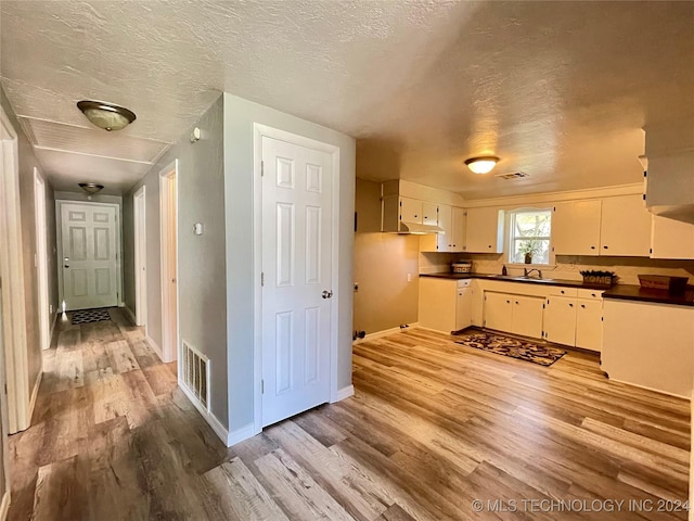 kitchen with white cabinets, a textured ceiling, and light hardwood / wood-style flooring