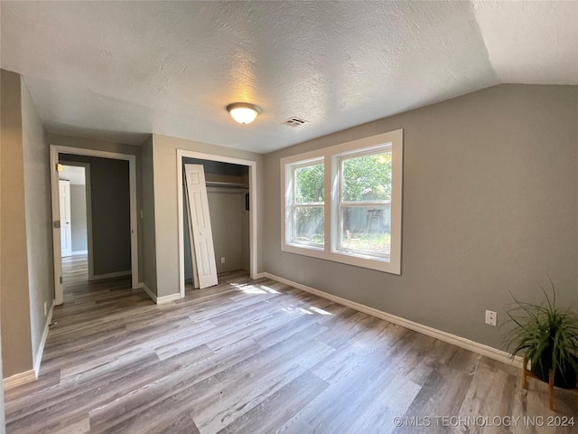 unfurnished bedroom featuring a closet, light wood-type flooring, a textured ceiling, and vaulted ceiling