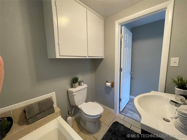 bathroom with toilet, a textured ceiling, tile patterned floors, and sink