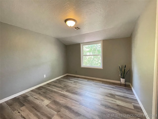 empty room with hardwood / wood-style floors, a textured ceiling, and vaulted ceiling