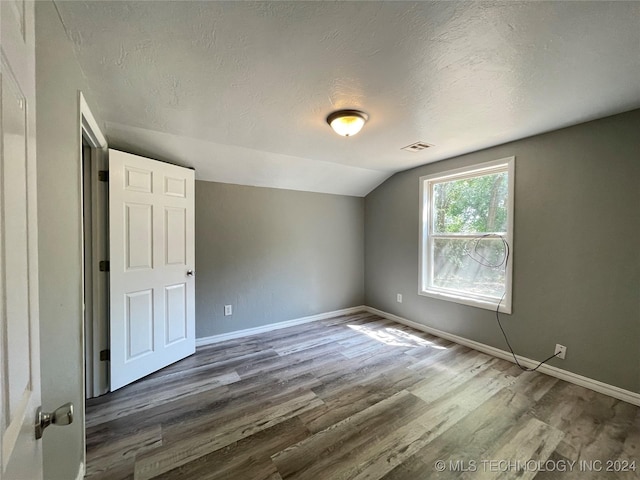 additional living space featuring a textured ceiling, dark wood-type flooring, and lofted ceiling