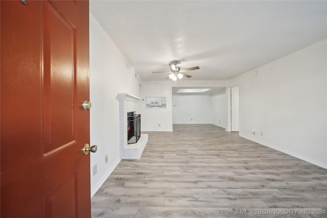 unfurnished living room with light wood-type flooring, a brick fireplace, and ceiling fan