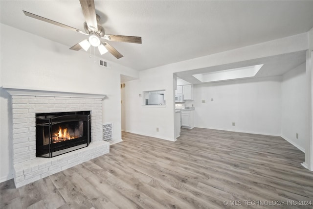 unfurnished living room featuring a skylight, ceiling fan, a fireplace, and light hardwood / wood-style floors