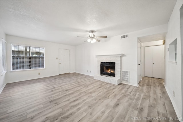 unfurnished living room with a fireplace, a textured ceiling, light hardwood / wood-style flooring, and ceiling fan