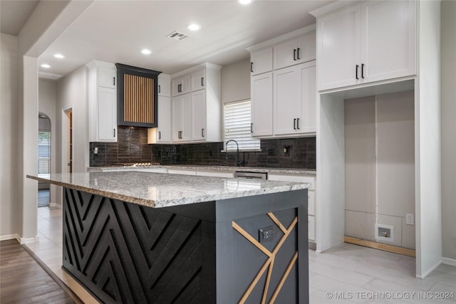 kitchen with white cabinets, light hardwood / wood-style floors, a kitchen island, and light stone counters