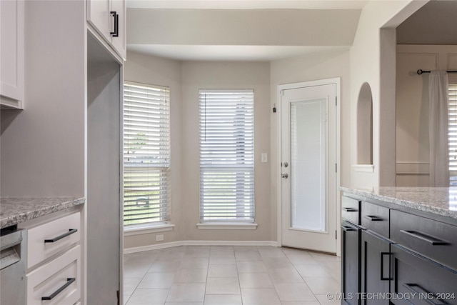 kitchen with light stone countertops, white cabinetry, dishwasher, and light tile patterned flooring