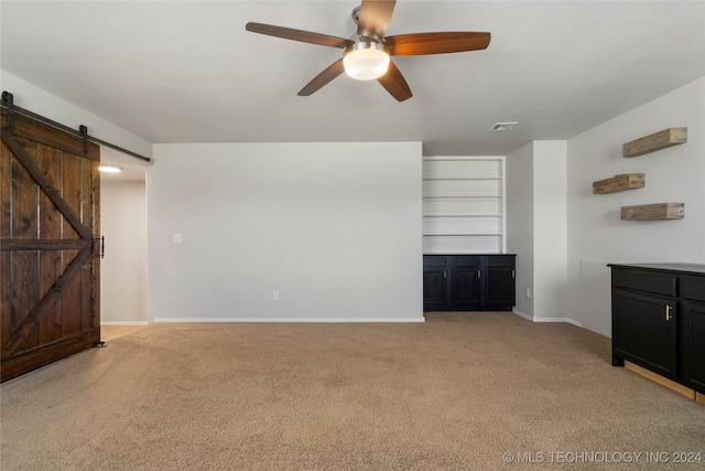 unfurnished living room featuring a barn door, ceiling fan, and light colored carpet