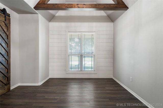 spare room featuring a barn door, wooden walls, dark wood-type flooring, and vaulted ceiling with beams