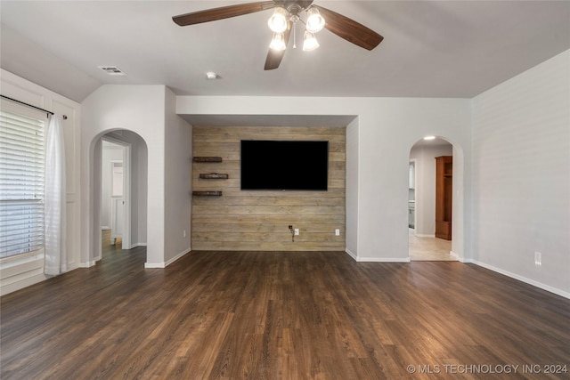 unfurnished living room featuring wood walls, dark hardwood / wood-style floors, ceiling fan, and a wealth of natural light