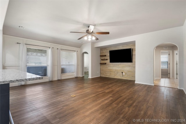 unfurnished living room with ceiling fan, dark hardwood / wood-style flooring, and wooden walls