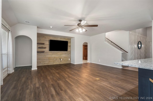 unfurnished living room featuring vaulted ceiling, ceiling fan, dark wood-type flooring, and wood walls