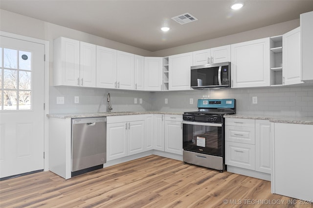 kitchen featuring white cabinets, appliances with stainless steel finishes, light wood-type flooring, and tasteful backsplash