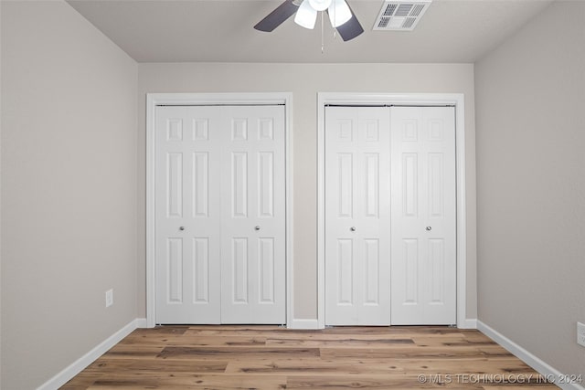 unfurnished bedroom with ceiling fan, wood-type flooring, and multiple closets