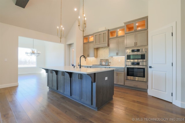 kitchen featuring a sink, stainless steel appliances, high vaulted ceiling, and a center island with sink