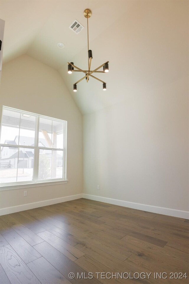 spare room with lofted ceiling, an inviting chandelier, and dark wood-type flooring