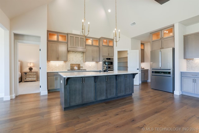 kitchen with pendant lighting, a large island with sink, high vaulted ceiling, appliances with stainless steel finishes, and dark hardwood / wood-style flooring