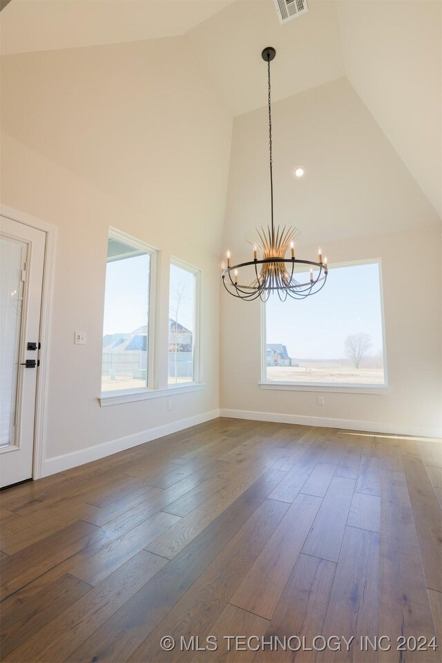 unfurnished dining area with dark wood-type flooring, high vaulted ceiling, and an inviting chandelier