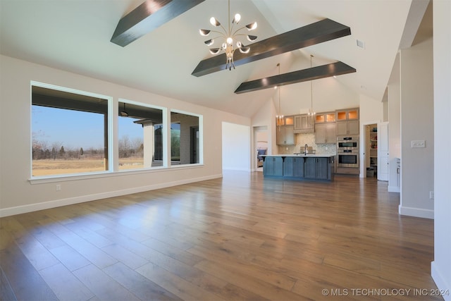 unfurnished living room featuring dark wood-type flooring, baseboards, a chandelier, beam ceiling, and a sink