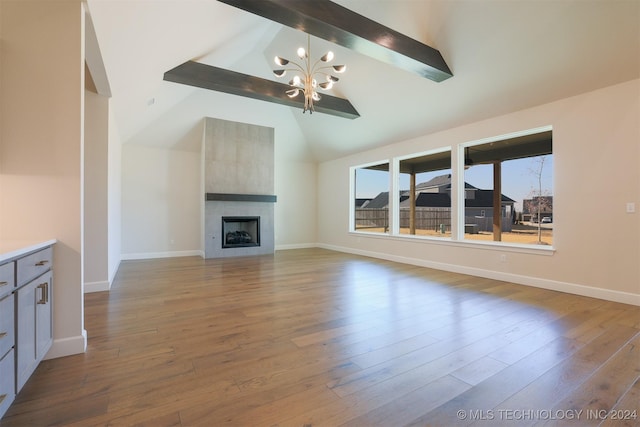 unfurnished living room with a notable chandelier, wood finished floors, vaulted ceiling with beams, and a tile fireplace