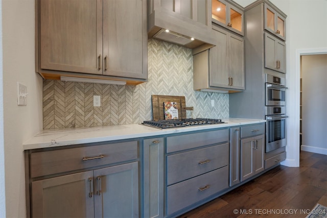 kitchen with custom range hood, tasteful backsplash, dark wood-style floors, appliances with stainless steel finishes, and light stone countertops