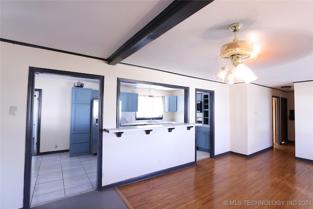 kitchen featuring hardwood / wood-style floors, blue cabinets, ceiling fan, a textured ceiling, and beamed ceiling